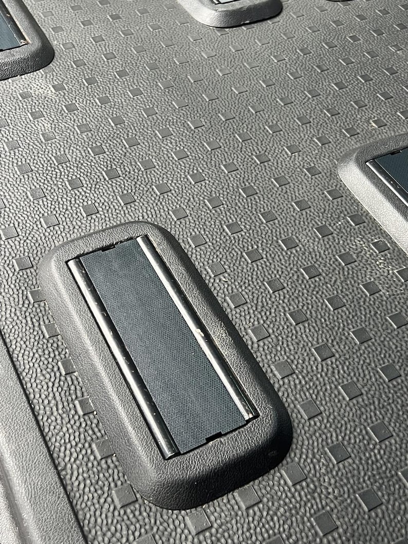 May include: Close-up of a black plastic cargo liner with a textured surface and a rectangular cutout with a black rubber strip.