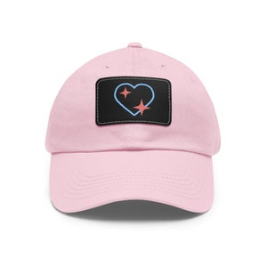 May include: A pink baseball cap with a black patch featuring a blue heart with two pink stars.
