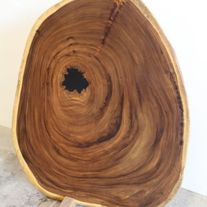 May include: A large, oval-shaped wooden slab with a natural edge and a knot hole in the center. The slab is resting on two wooden blocks and a wooden dowel.