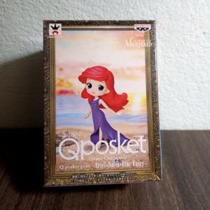 May include: A boxed Q Posket figure of Ariel from Disney's The Little Mermaid. The figure has red hair and a purple dress. The box features the figure in front of a beach scene and includes the text "Q posket petit - Ariel-Sofia-Blue Fairy-".