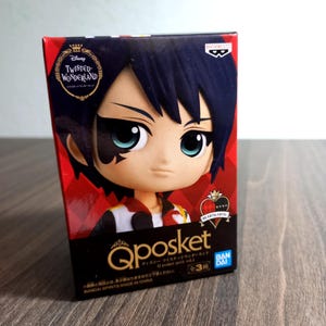 May include: A rectangular cardboard box featuring a Disney Twisted-Wonderland Q posket petit figure. The box displays a character with dark hair, large teal eyes, and a heart-shaped mark on the face. Text includes Qposket, Banpresto, and Bandai.