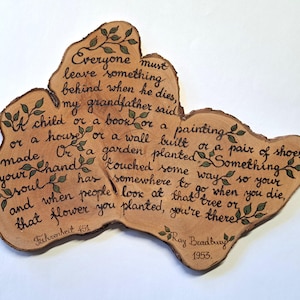 Może przedstawiać: Drewniana tablica z cytatem z książki Fahrenheit 451 Raya Bradbury'ego, ręcznie napisanym czarnym tuszem. Cytat otoczony jest zielonymi akcentami liści. Tablica ma kształt przekroju drzewa.