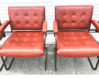 May include: Four red leather chairs with metal frames. The chairs have a tufted design and are arranged in a row.