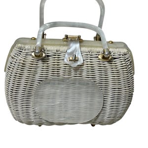 May include: A vintage white wicker handbag with a clear plastic handle and clasp. The oval-shaped front panel is also clear plastic. The bag has gold-colored metal accents and a woven texture.