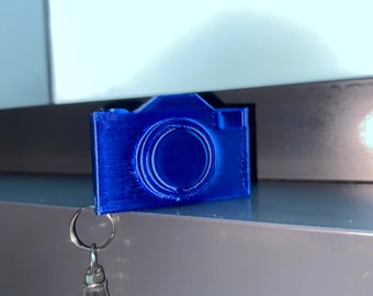 May include: A blue plastic camera keyring with a silver metal clasp.