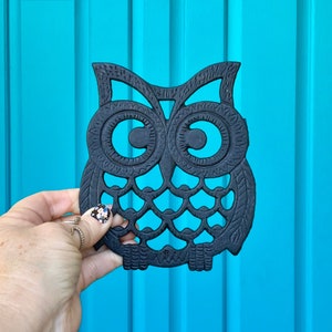 May include: Black cast iron owl-shaped hot pad. The owl has large, round eyes and a detailed design.