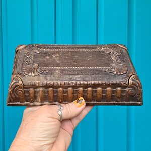 May include: A vintage wooden box with intricate carvings and a dark brown finish. The box has a hinged lid and a decorative design on the front.