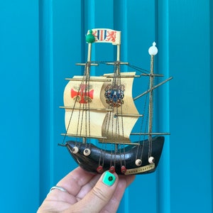 May include: A small wooden model ship with black and white sails and a black hull. The ship has a green and white flag with a red lion on it. The ship is labeled "Bremerhaven".