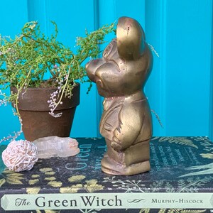 Op de afbeelding: Een messing beeldje van een muis in een pak. Het beeldje staat op een stapel boeken met de titel "The Green Witch".