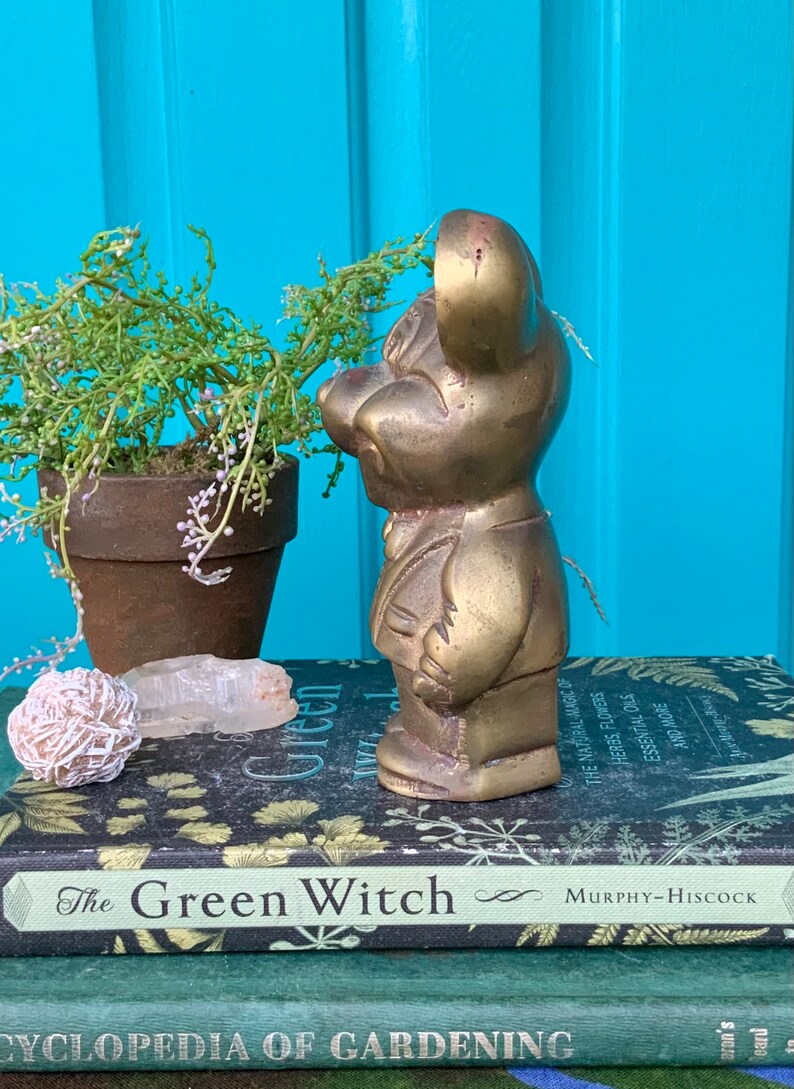 Op de afbeelding: Een messing beeldje van een muis in een pak. Het beeldje staat op een stapel boeken met de titel "The Green Witch".