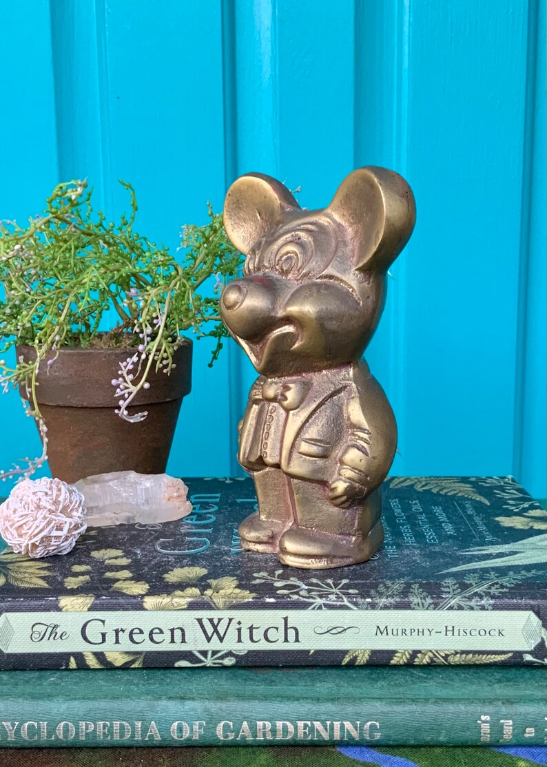 Op de afbeelding: Een messing beeldje van Mickey Mouse in smoking. Het beeldje staat op een stapel boeken met de titel "The Green Witch" zichtbaar.