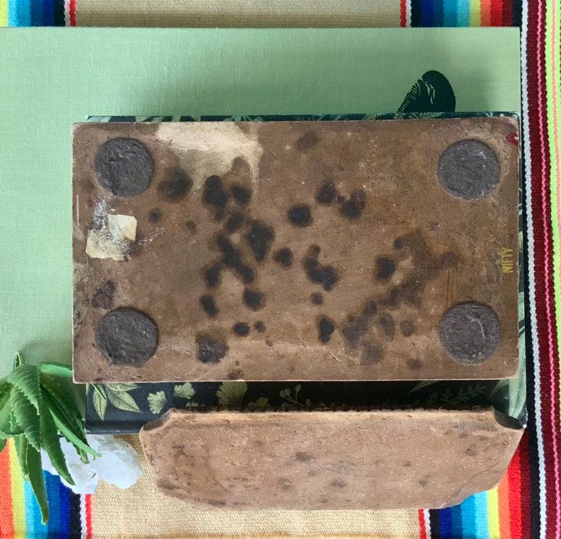 May include: Two rectangular brown ceramic tiles with a rough texture. The top tile has four black metal circles attached to the bottom. The bottom tile has the word "NIFTY" printed on the right side.