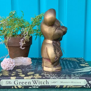 Op de afbeelding: Een gouden metalen beeldje van een beer in een pak. De beer staat op een stapel boeken met de titel "The Green Witch".
