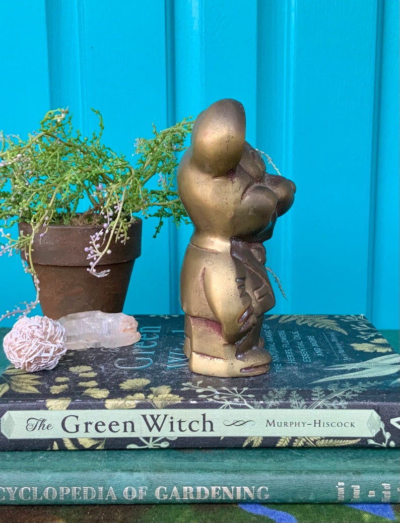 Op de afbeelding: Een gouden metalen beeldje van een beer in een pak. De beer staat op een stapel boeken met de titel "The Green Witch".