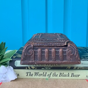 May include: A vintage wooden box with intricate carvings and a hinged lid. The box is resting on top of a stack of books.