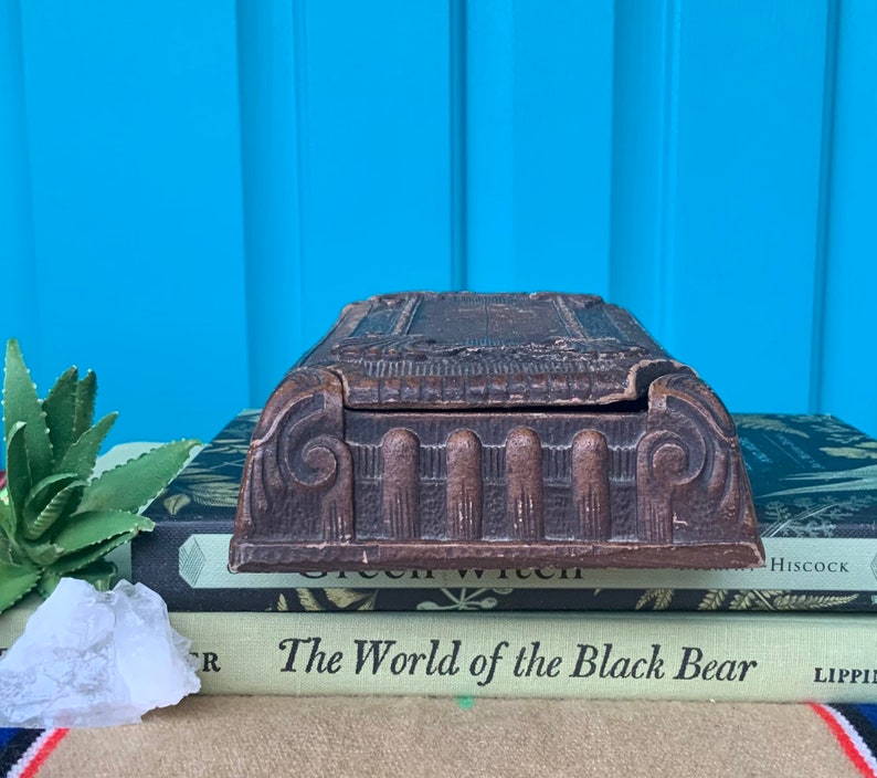 May include: A vintage wooden box with intricate carvings and a hinged lid. The box is resting on top of a stack of books.