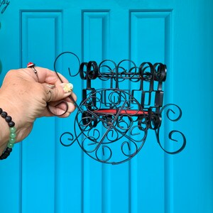 May include: Black metal wine rack with a red shelf and intricate scrollwork design. The rack is hanging on a blue door.
