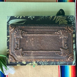 May include: A vintage, ornate, dark brown wooden box with intricate carvings and a raised, rectangular design. The box is closed and has a slightly distressed finish.