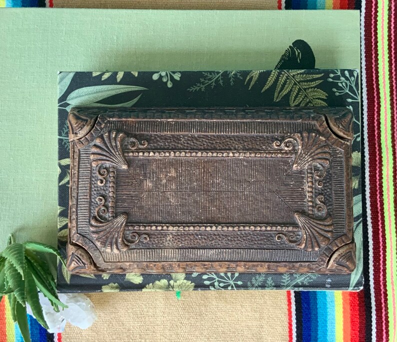 May include: A vintage, ornate, dark brown wooden box with intricate carvings and a raised, rectangular design. The box is closed and has a slightly distressed finish.