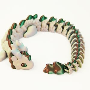 May include: A whimsical, articulated dragon figurine in shades of white, green, and brown. The dragon has a detailed, segmented body and a cute, expressive face. The toy is designed to be flexible and poseable.