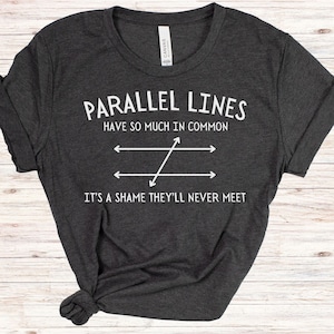 May include: A dark gray t-shirt with a white graphic that says "Parallel Lines Have So Much In Common It's A Shame They'll Never Meet". The graphic also includes a diagram of two parallel lines with a diagonal line intersecting them.