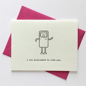 May include: A white card with a black and white pixelated robot illustration and the text "I was programmed to like you."
