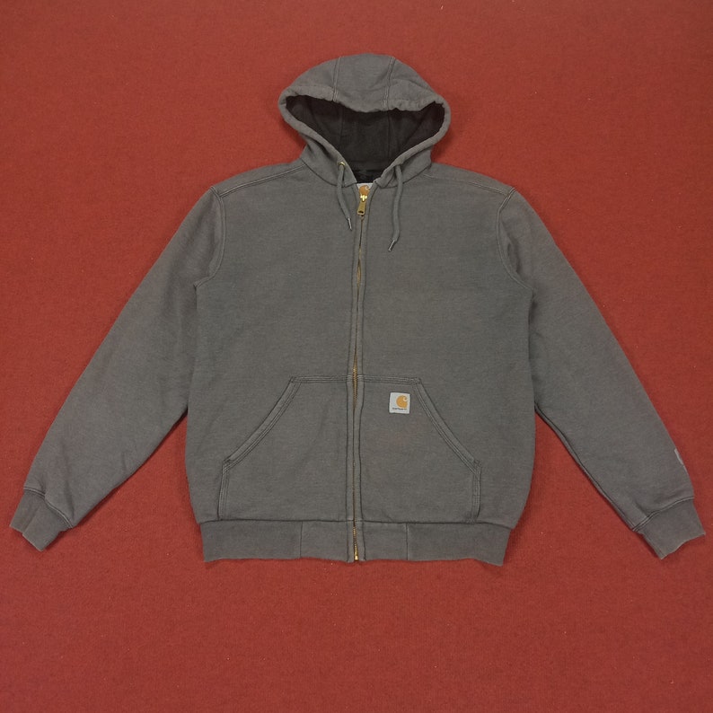 May include: A gray zip-up hooded sweatshirt with a Carhartt logo patch on the left chest. The sweatshirt has a kangaroo pocket and a drawstring hood.