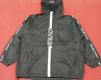 May include: Black hooded jacket with a white stripe down the front and "KANI" written in white on the stripe. The jacket has a zipper closure and a pocket on the left side. The sleeves and bottom of the jacket have white "KANI SPORT" text repeated along the edges.