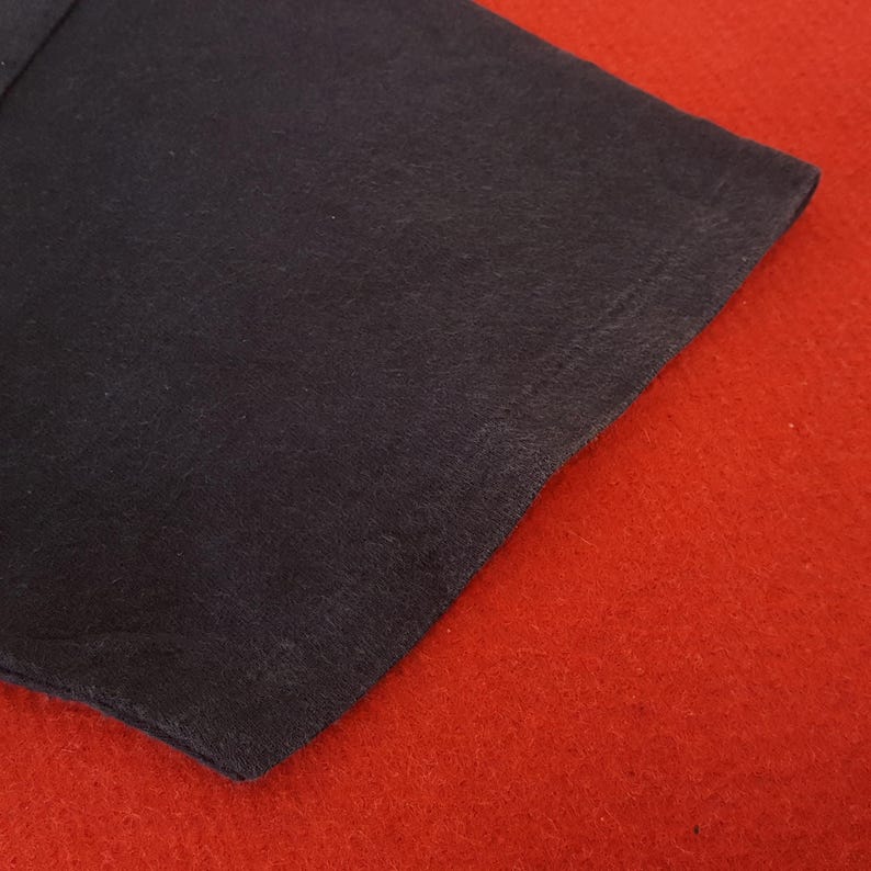 May include: A close-up of a dark navy blue fabric corner against a vibrant red background. The fabric appears to be soft and textured, with a slight sheen. The red background provides a striking contrast to the dark fabric.