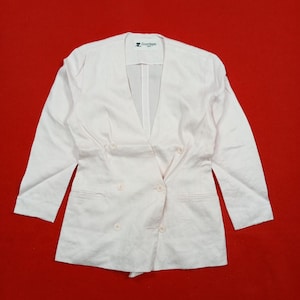 May include: A light pink double-breasted blazer with a V-neckline and three-quarter sleeves. The blazer has two rows of buttons and a tailored fit. The Courreges logo is visible on the upper left side of the blazer.