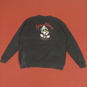 Puede incluir: Sudadera negra con un gráfico bordado en rojo de un personaje de dibujos animados jugando a los bolos con el texto "Gouge Clothing" en la espalda.