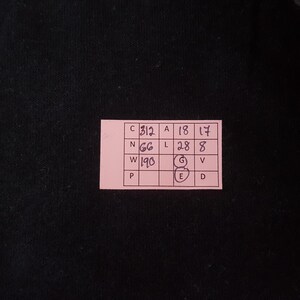 May include: A pink rectangular tag with black text and numbers. The tag is on a black background. The text includes the letters C, N, W, P, A, L, G, E, V, and D, along with the numbers 312, 66, 190, 18, 28, 17, and 8.