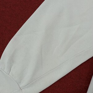 May include: Close-up of a light gray sweatshirt sleeve. The sleeve is made of a soft, textured fabric and features a ribbed cuff. The background is a deep red color.