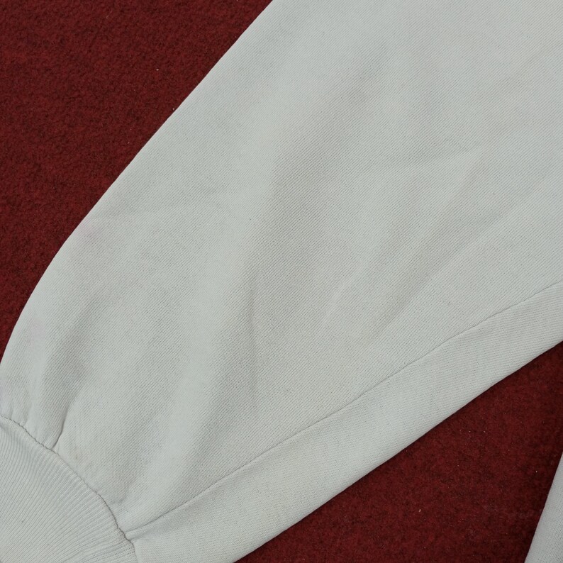 May include: Close-up of a light gray sweatshirt sleeve. The sleeve is made of a soft, textured fabric and features a ribbed cuff. The background is a deep red color.