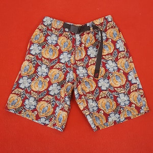 May include: Shorts featuring a colourful floral design in orange, blue, and white on a burgundy backdrop. They have a black belt and buckle. The shorts are made of a lightweight material.