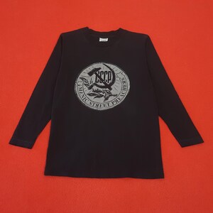 May include: Black long-sleeve shirt with a circular graphic featuring a hammer and sickle, wheat, and the text "UNIC STREET PREACHERS" and "CCCP". The shirt is on a red background.