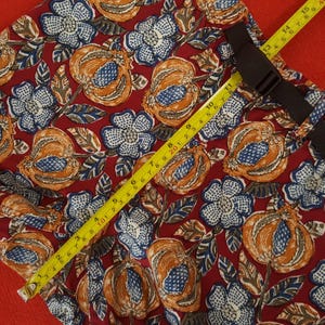 May include: Red fabric with a floral design of orange, blue, and white flowers and fruit. A yellow measuring tape indicates a length of approximately 38 cm. A black strap is also visible.