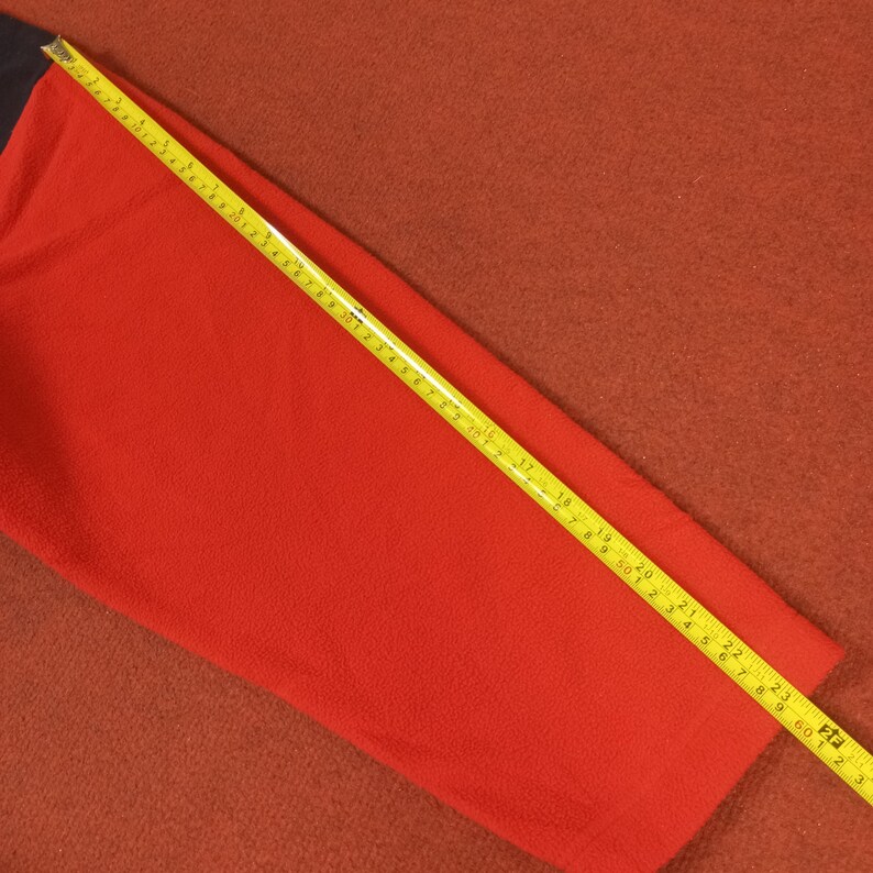 May include: A red fleece sleeve with a yellow measuring tape laid across it. The tape measures 25 inches.