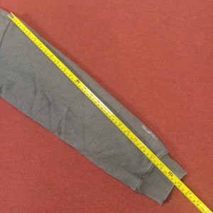 May include: A gray sweatshirt sleeve with a yellow measuring tape showing a length of 23 inches.