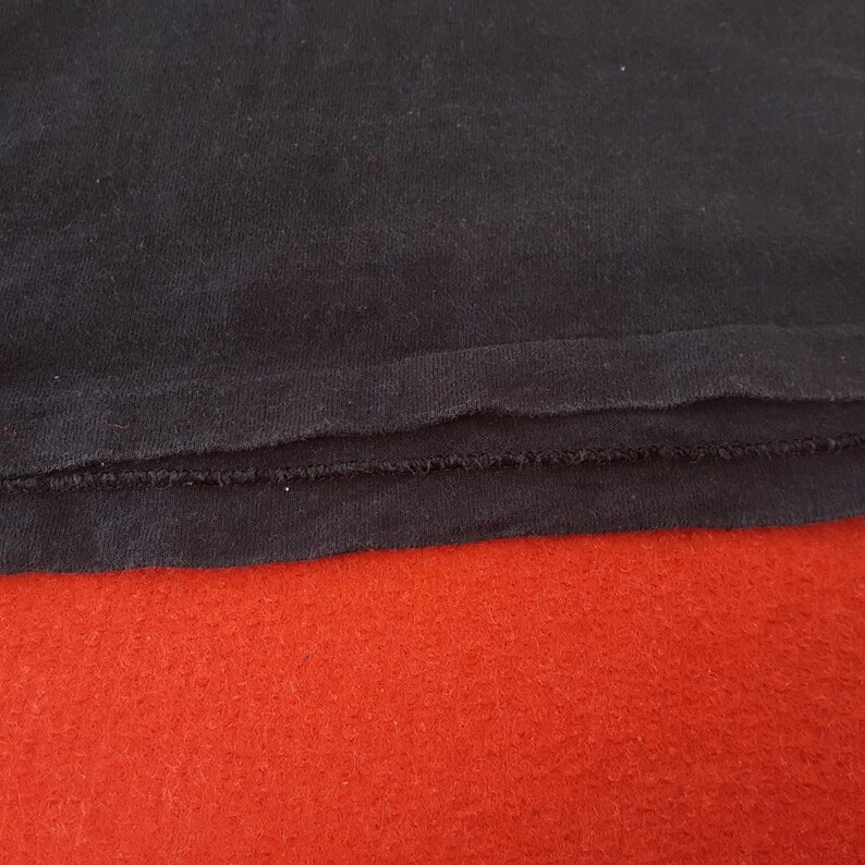 May include: Close-up of a dark navy blue fabric with a raw, unfinished edge. The fabric is layered over a vibrant red surface, creating a contrast in color and texture. The image highlights the details of the textile.