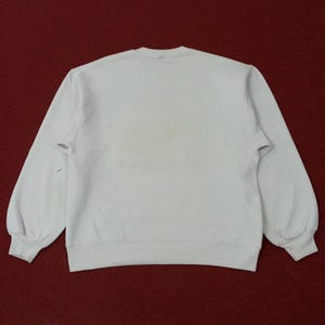 May include: A light-colored sweatshirt with long sleeves, viewed from the back. The garment has a crew neck and ribbed cuffs and hem. There are some stains on the front of the sweatshirt. The background is a dark red.