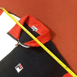 May include: A navy blue, red, and white zip-up jacket with a Fila logo on the collar and a Fila logo on the front.