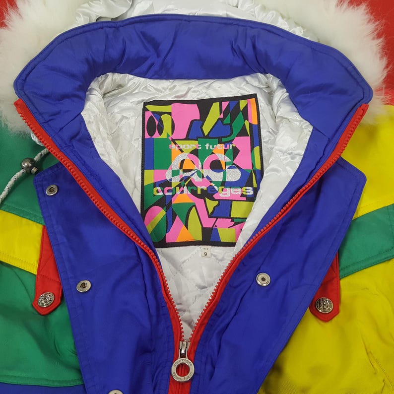 Puede incluir: Chaqueta de esqu&iacute; vintage colorida con cuello de piel sint&eacute;tica blanca. La chaqueta presenta un cuello azul, cremallera roja y detalles en verde y amarillo. El forro interior tiene un gr&aacute;fico colorido con el texto "acurr&egrave;ges".