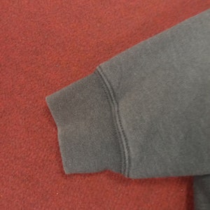 May include: Close-up of the dark gray fabric cuff of a sweatshirt. The cuff is folded over and stitched with a double row of stitching.