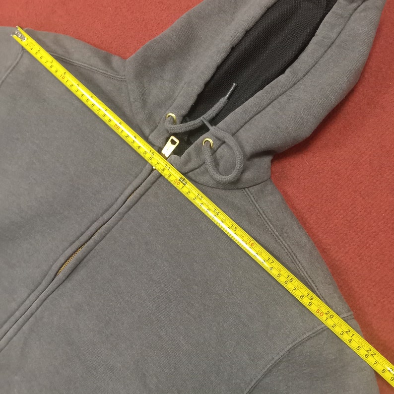 May include: A gray hooded sweatshirt with a zipper closure. The zipper is gold colored and the hood has a black mesh lining. A measuring tape is laid across the sweatshirt, showing the length of the zipper to be 22 inches.