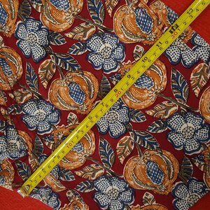May include: A fabric featuring a repeating pattern of orange fruit and blue and white flowers on a burgundy background. A yellow tape measure shows a measurement of 33 cm.
