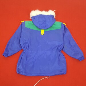Puede incluir: Chaqueta de invierno azul con capucha forrada de piel sint&eacute;tica blanca. La chaqueta presenta detalles verdes y amarillos en los hombros y una franja roja en las mangas. Tiene cintura con cord&oacute;n y cierre de bot&oacute;n a presi&oacute;n amarillo.