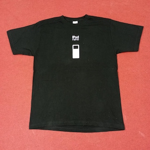 Pode incluir: Camiseta preta com as palavras "iPod nano" acima de um gráfico de retângulo branco. A camiseta de manga curta é feita de um material macio. A camiseta é exibida em uma superfície vermelha.