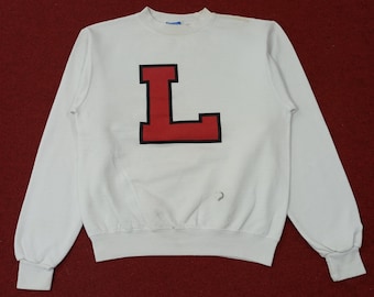 May include: White sweatshirt with a large red and black letter "L" on the front. The long-sleeved top has a crew neck and ribbed cuffs. The sweatshirt is made of a soft material and is likely vintage.