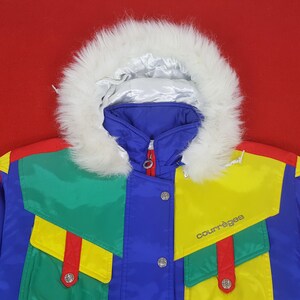 Puede incluir: Chaqueta de invierno vintage colorida con capucha de piel sint&eacute;tica blanca. La chaqueta presenta un cuerpo azul, detalles amarillos y verdes y ribetes rojos. El nombre de la marca "Courr&egrave;ges" est&aacute; impreso en la parte delantera.